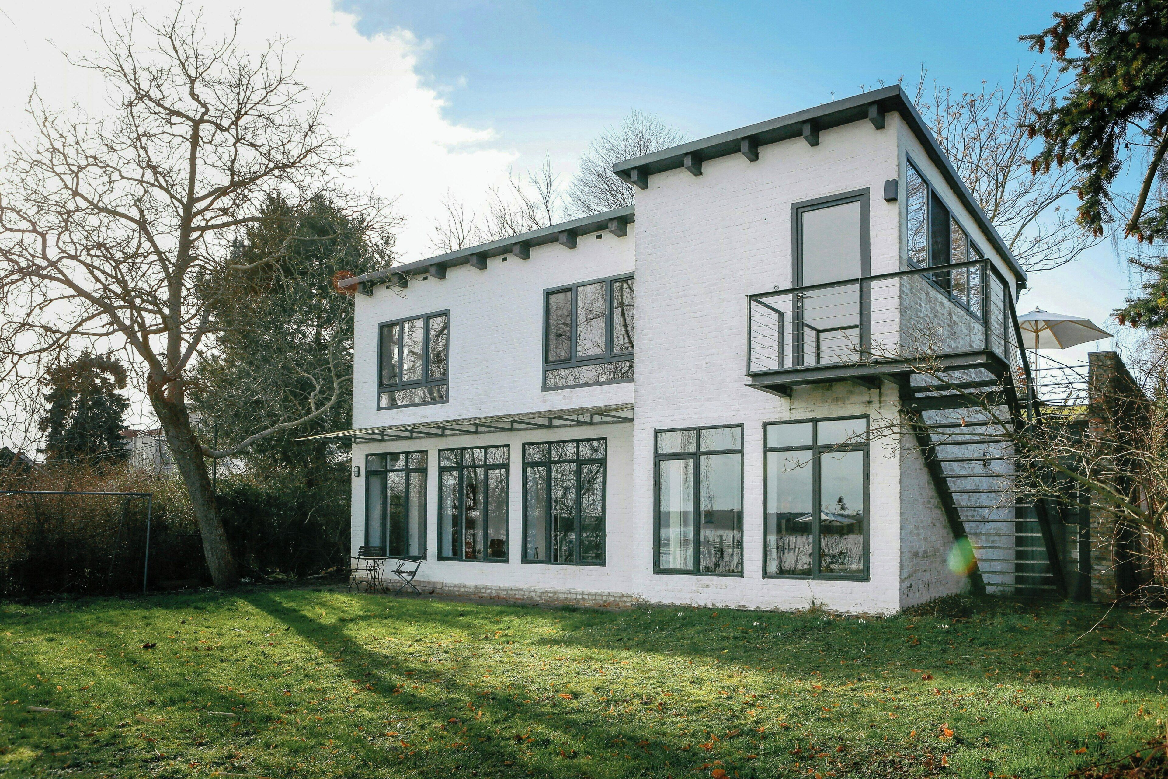 Een modern huis met twee verdiepingen, grote ramen, een balkon en een zichtbare trap.