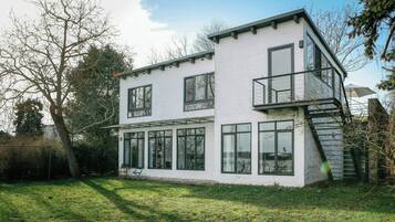 Een modern huis met twee verdiepingen, grote ramen, een balkon en een zichtbare trap.
