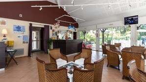 Un vestíbulo de hotel con mobiliario de mimbre, una zona de bar y una pantalla de televisión.