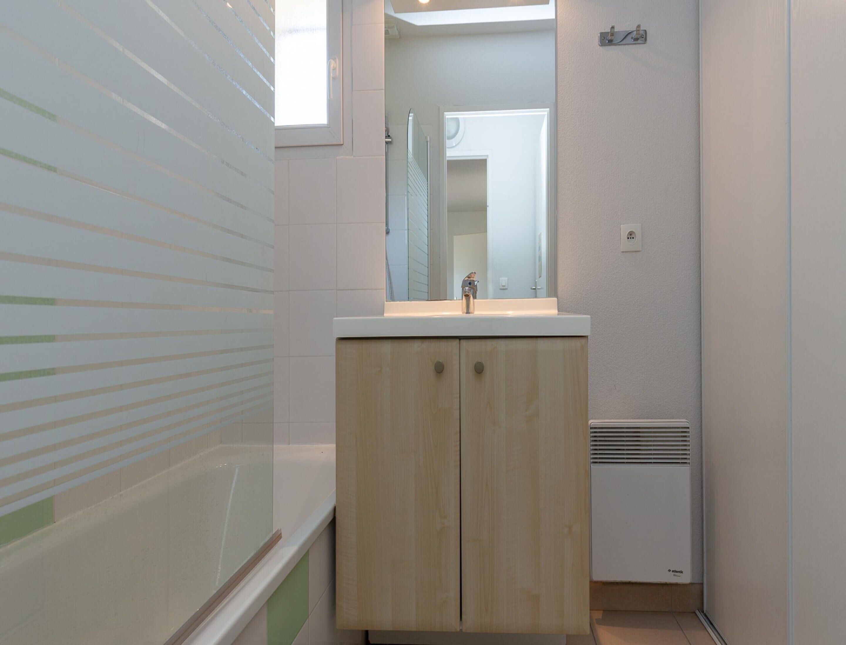 Une salle de bain avec un meuble en bois, un lavabo blanc, un miroir et une fenêtre.