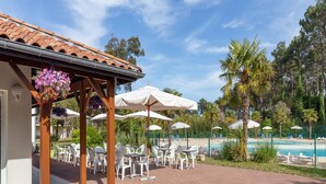 Zona de piscina con mobiliario exterior, sombrillas y una pérgola decorada con flores colgantes.
