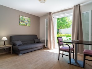A modern room with a grey sofa, a small table, a chair, and a window with curtains. - Decent Stay in Art Village With Terrace (Pont-Aven)