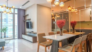 A modern kitchen with a dining area, large windows, and a flat-screen TV. - The Grand K-Vinhomes - Stunning Views (Ho Chi Minh City)