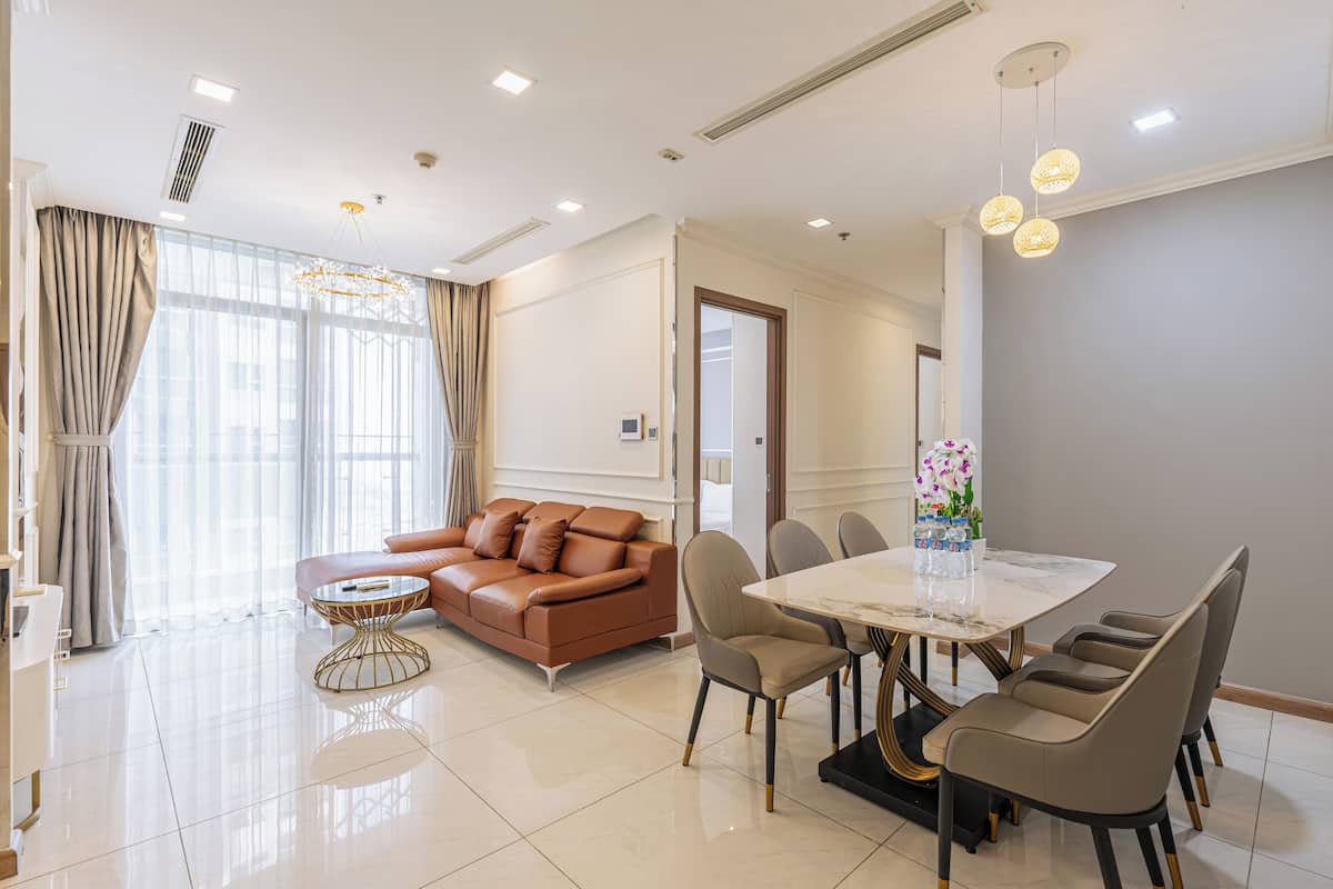 Una sala de estar moderna con un sofá de cuero marrón, una mesa redonda y un comedor con mesa y sillas blancas.
