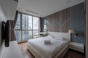 A modern hotel room with a large bed, a TV, a desk, a lamp, and a view of the cityscape. - The Grand K-Vinhomes - Stunning Views (Thanh My Tay)