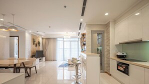 A modern kitchen with a built-in oven, a dining area with a table and chairs, and a bar area with stools. - The Grand K-Vinhomes - Stunning Views (Ho Chi Minh City)