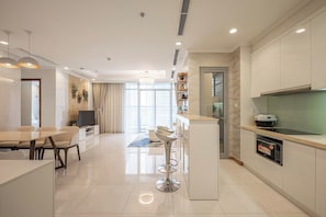 A modern kitchen with a built-in oven, a dining area with a table and chairs, and a bar area with stools. - The Grand K-Vinhomes - Stunning Views (Thanh My Tay)