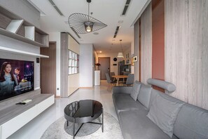 A modern living room with a flat-screen TV, a round coffee table, a grey sofa, and a dining area in the background. - The Grand K-Vinhomes - Stunning Views (Thanh My Tay)