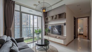 A modern living room with a sofa, TV, and large windows overlooking a cityscape. - The Grand K-Vinhomes - Stunning Views (Ho Chi Minh City)