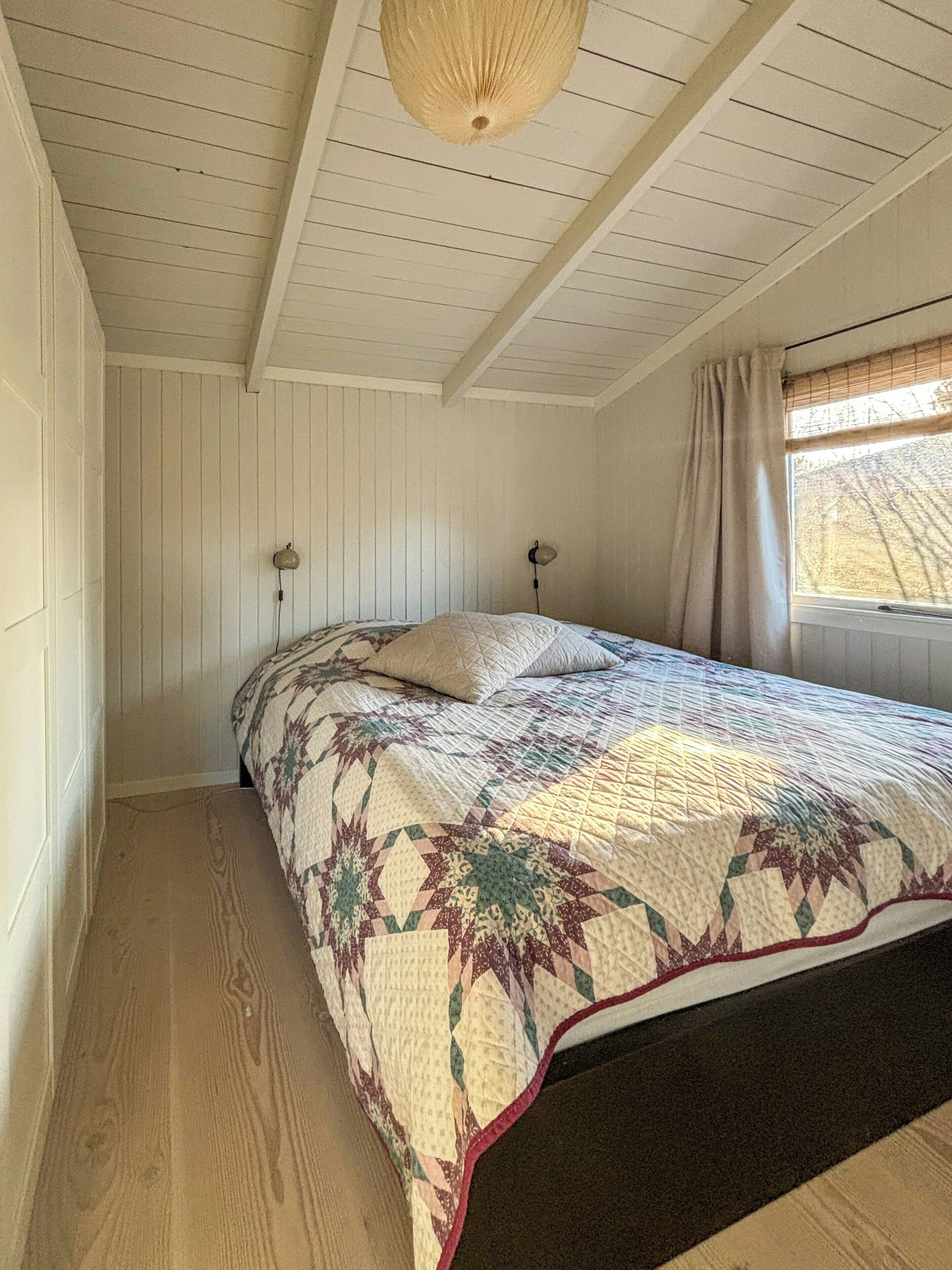 Ein Schlafzimmer mit Bett, Fenster mit Vorhängen und einer Deckenleuchte.