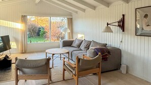 Ett rymligt vardagsrum med högt tak, synliga träbjälkar, en soffgrupp, ett soffbord och en tv.