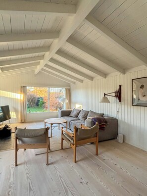 Ein geräumiges Wohnzimmer mit hoher Decke, Holzbalken, einer Sofagarnitur, einem Couchtisch und einem Fernseher.