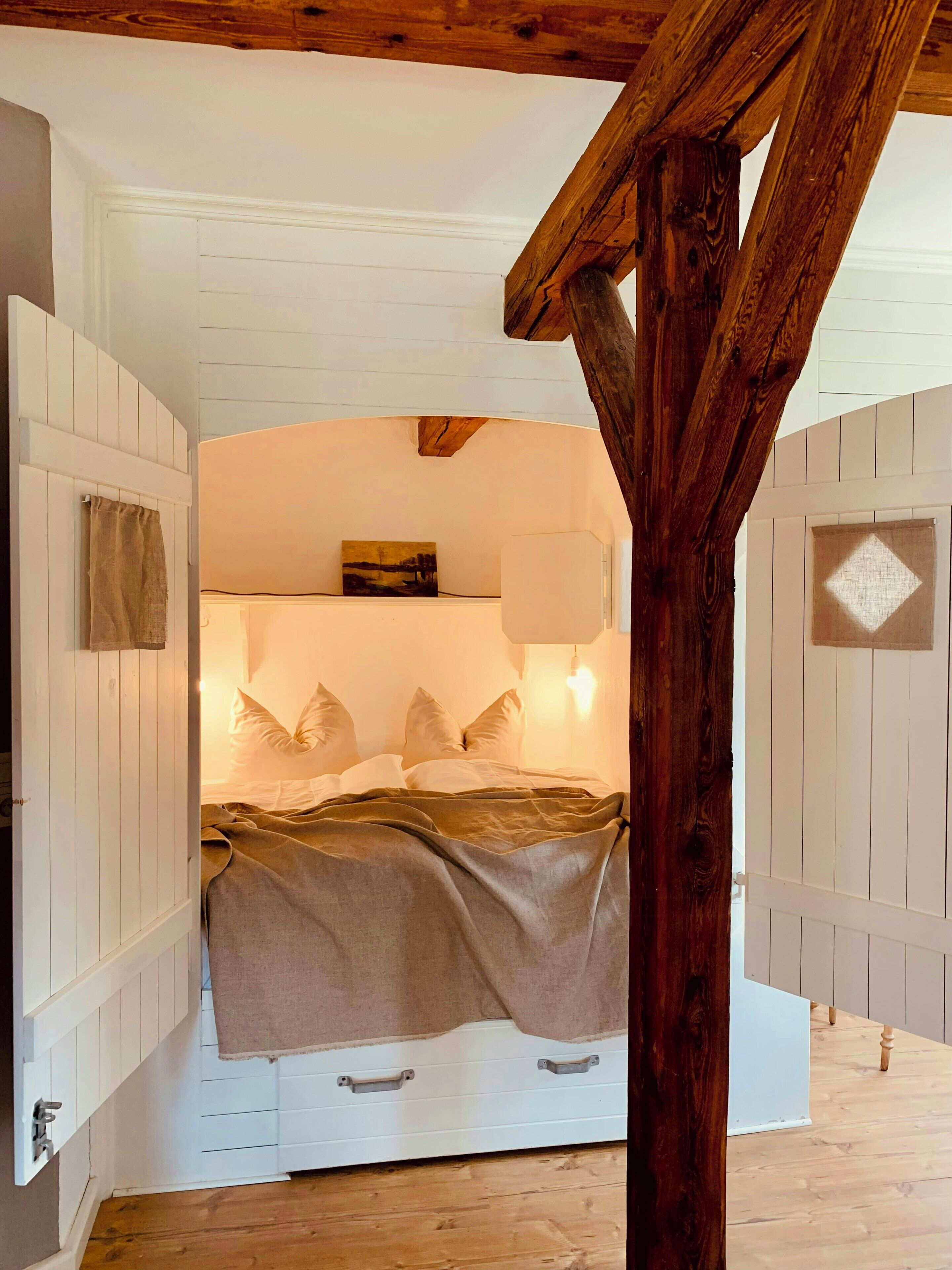 Une chambre à coucher avec un lit, des oreillers, un tableau et une poutre en bois au plafond.