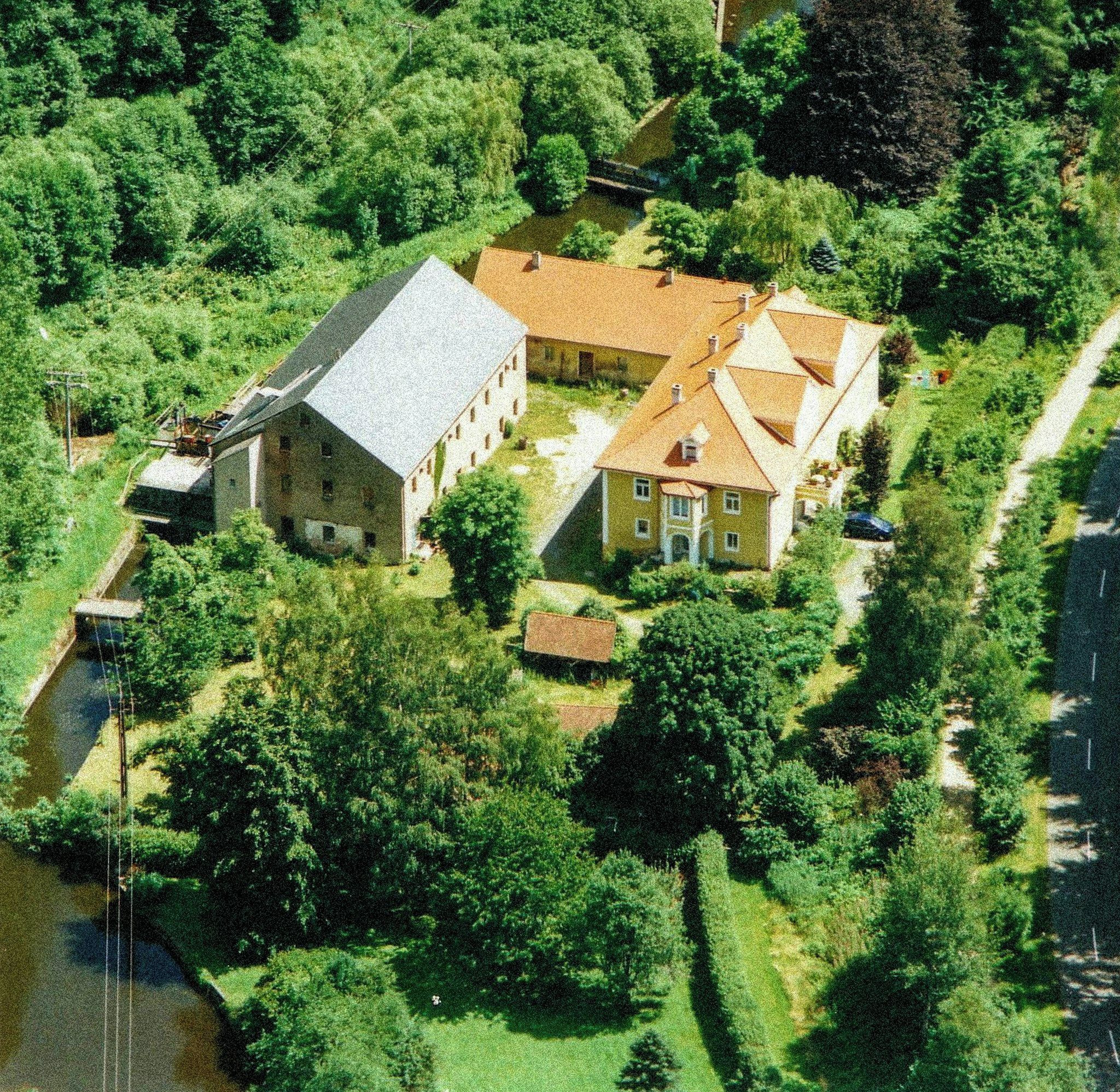 Un vaste domaine comprenant plusieurs bâtiments, une rivière et une végétation luxuriante.