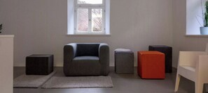 A modern living room with a grey armchair, a striped ottoman, a red cube-shaped ottoman, and a white chair. - Minimalist style apartment in Upper Palatinate (Neuenburg vorm Wald)