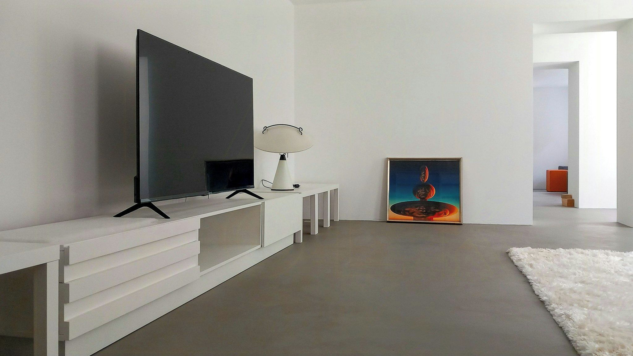 Una sala de estar moderna con un televisor de pantalla plana, un elegante aparador blanco, una lámpara de pie y un cuadro en la pared.