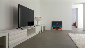 A modern living room with a flat-screen TV, a white console table, a floor lamp, and a painting on the wall. - Minimalist style apartment in Upper Palatinate (Neuenburg vorm Wald)