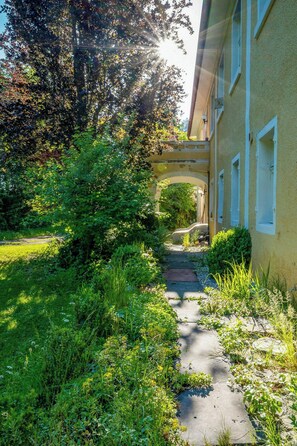 A pathway leading to a building with a covered entrance, surrounded by lush greenery and a clear sky. - Minimalist style apartment in Upper Palatinate (Neuenburg vorm Wald)