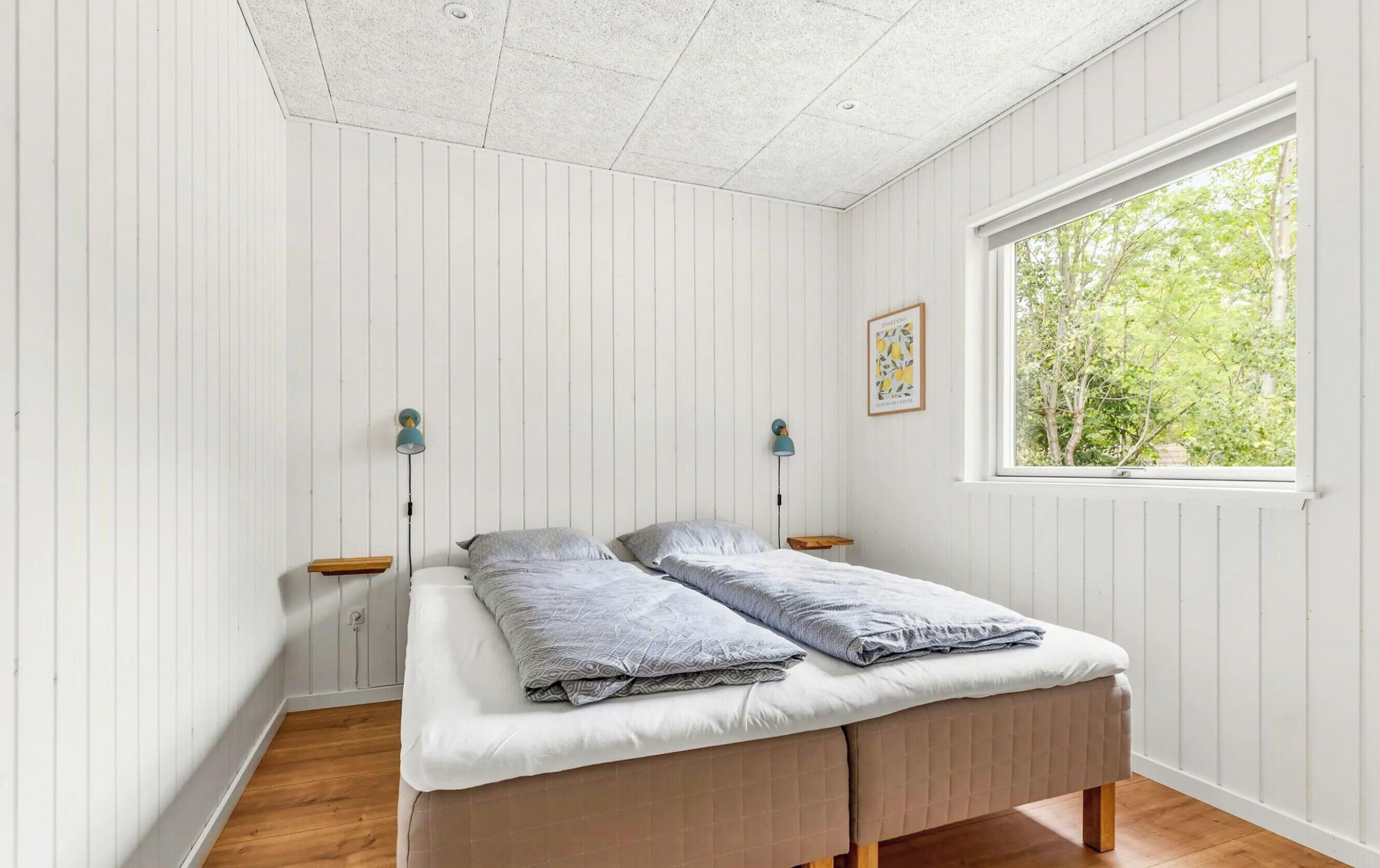 A bedroom with a bed, two bedside tables, a window with a view of trees, and a ceiling with a grid pattern.