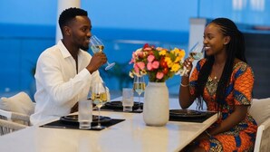A dining table with two people seated, each holding a wine glass. There is a vase with colorful flowers on the table. - Hayce Residence Nyali (Mombasa)