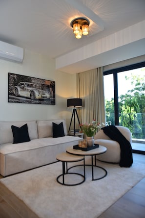 Ein modernes Wohnzimmer mit einer Couch, einem Couchtisch, einer Stehlampe und einem großen Fenster mit Blick auf Grünflächen.