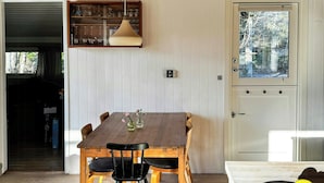A dining area with a wooden table and chairs, a pendant light, and a view through a door. - Charming family summerhouse near the beach (Højby)