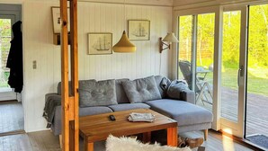 A modern living room with a wooden ceiling, a grey sofa, a wooden coffee table, and a white furry chair. - Charming family summerhouse near the beach (Højby)