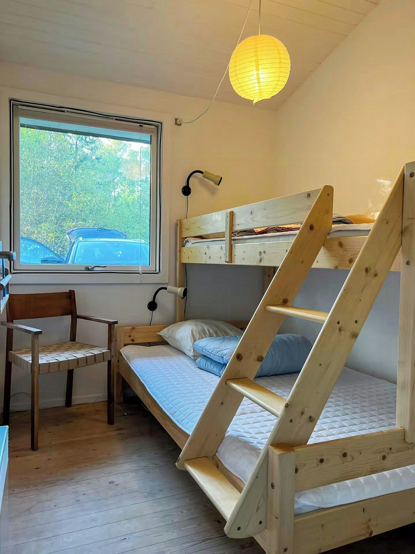 A bunk bed with a desk and chair, a lamp, and a window with a view of trees.