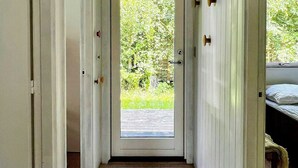 A hallway with a wooden floor, a door leading to a garden, and a bed with a white headboard in the background. - Charming family summerhouse near the beach (Højby)
