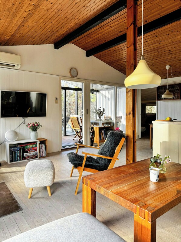 A modern living room with a wooden dining table, a fluffy chair, a sofa, and a TV mounted on the wall.