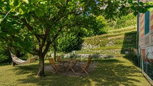 Une terrasse avec une table et des chaises, entourée de pelouse et d’arbres.