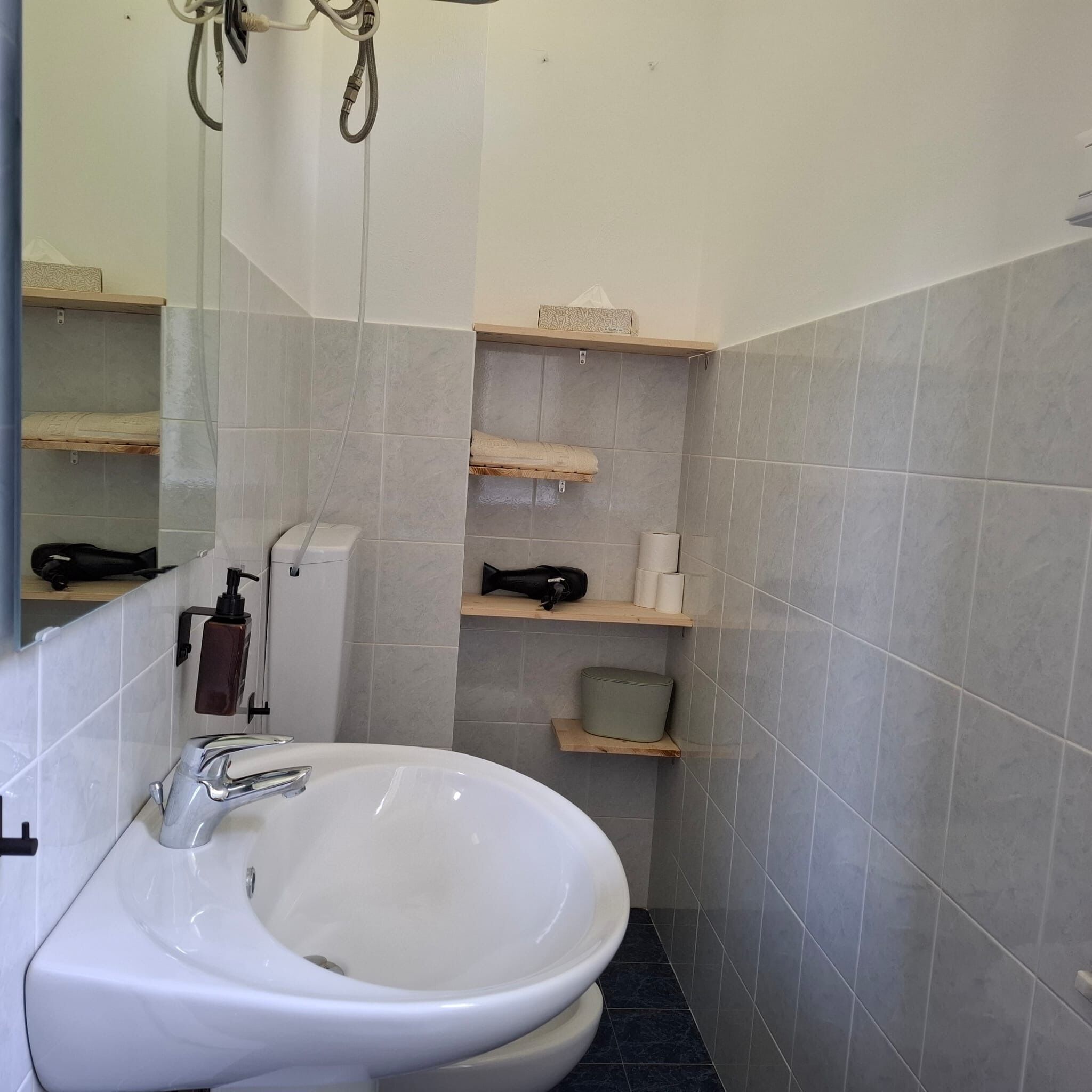 A bathroom with a white sink, a mirror, and shelves with toiletries.