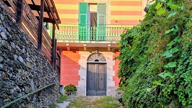 Une étroite ruelle pavée qui mène à un bâtiment dont un côté est bordé d’un mur de pierre et l’autre d’une clôture verte.