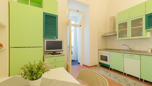 Une cuisine de taille réduite avec des meubles de couleur verte, une table à manger agrémentée d’une plante et un téléviseur.