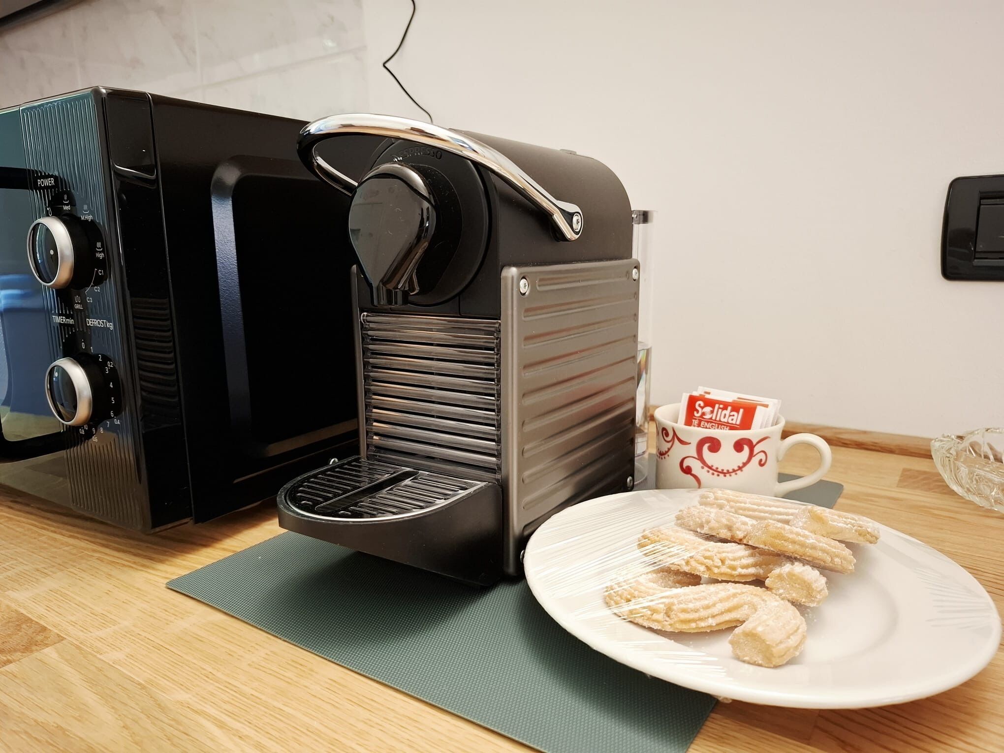 Une machine à café, une assiette de viennoiseries et une tasse de café sur une table.