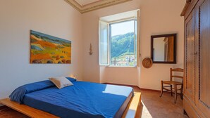 Une chambre à coucher avec un lit, une fenêtre donnant sur un beau paysage, un tableau et une armoire en bois.