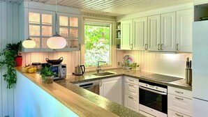 Una cocina con armarios blancos, encimera de madera, ventana con vistas a zonas verdes y un lavabo.