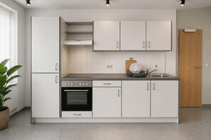 Cozinha moderna com armários brancos, forno embutido, bancada com pia e porta de madeira.