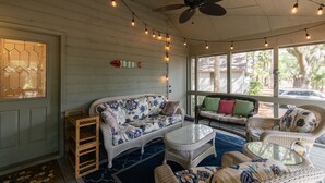 A covered porch with wicker furniture, a ceiling fan, string lights, and a view of the outdoors.