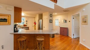 A kitchen with a central island, wooden flooring, and a dining area with two wicker chairs.