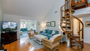 A spacious living room with a wooden staircase, a television, a sofa, and a coffee table.