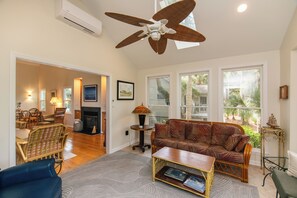 A living room with a ceiling fan, a fireplace, a sofa, a coffee table, and a dining area with chairs.