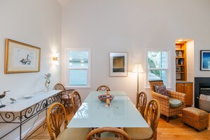 A dining area with a glass table, wicker chairs, a fireplace, and a bookshelf.