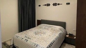 Een slaapkamer met een bed, een nachtkastje, een wandlamp en een ventilatie rooster in het plafond.