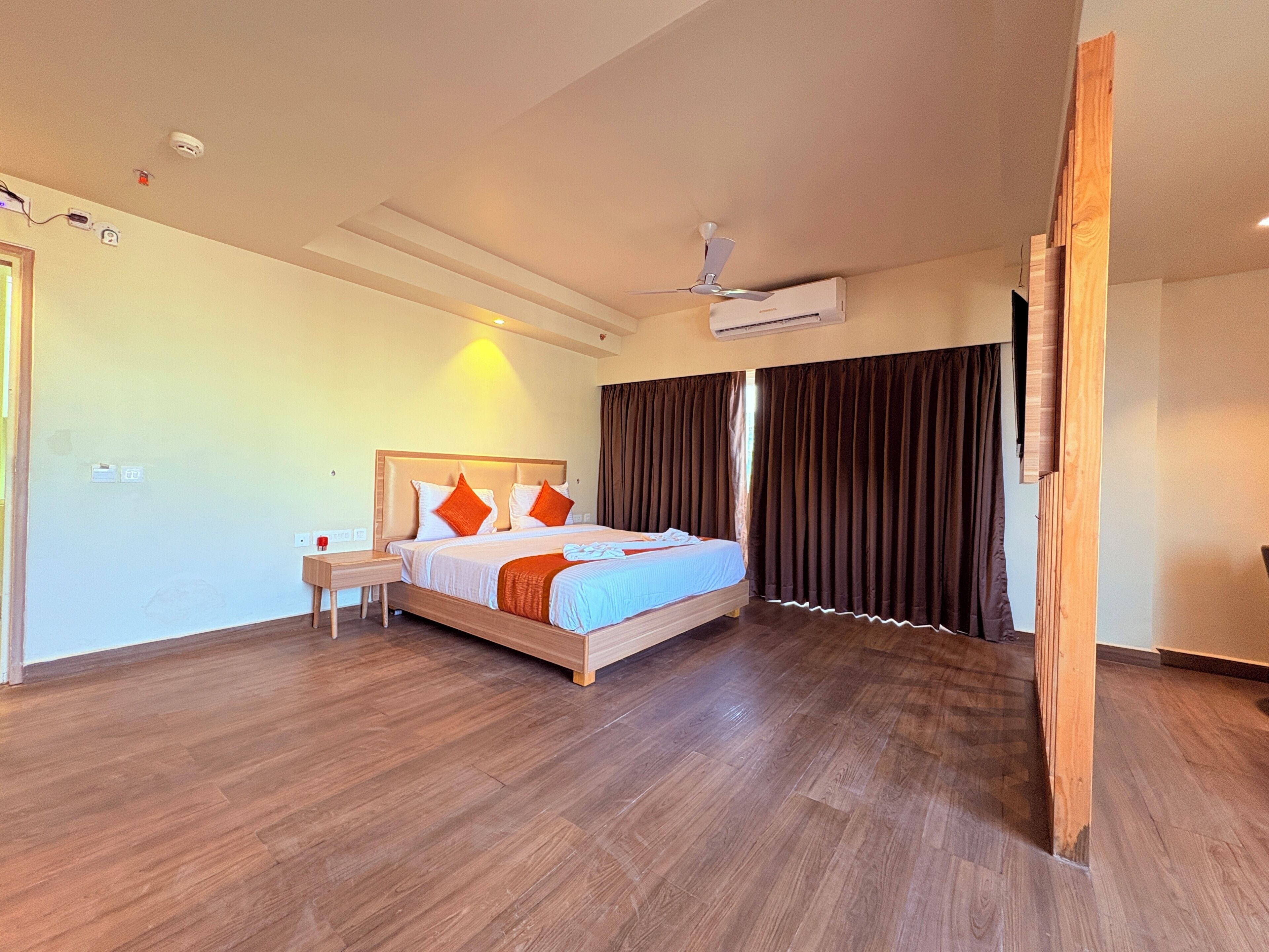 A modern hotel room with a wooden floor, a bed with orange and white bedding, a nightstand, and an air conditioning unit.
