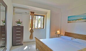 A bedroom with a bed, a dresser, a window with curtains, a lamp, and a painting on the wall. - Villa with ancient olive tree near Punta Secca (Kaukana, Santa Croce Camerina)
