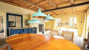 Un comedor amplio con mesa y sillas de madera, una cocina con armarios azules y lámparas colgantes de cobre.