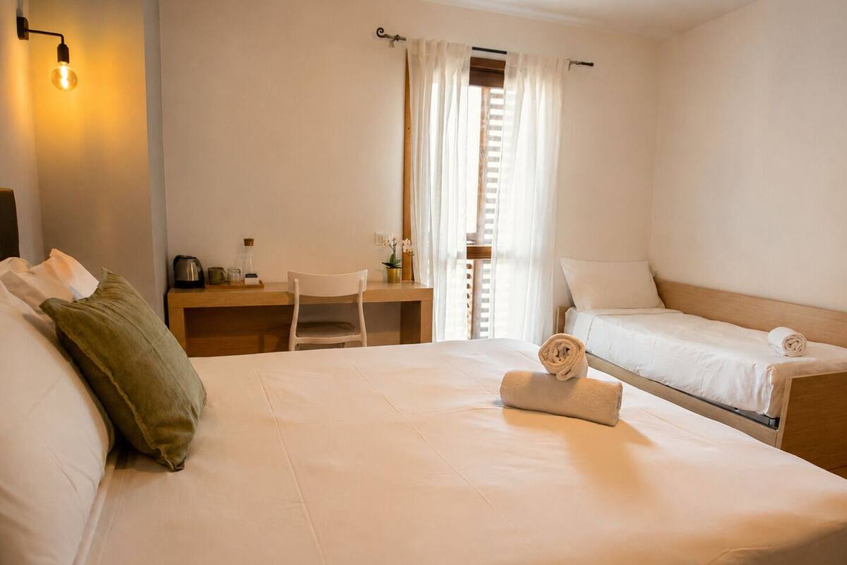 A hotel room with a bed, a desk, a chair, a small table, and a window with curtains.