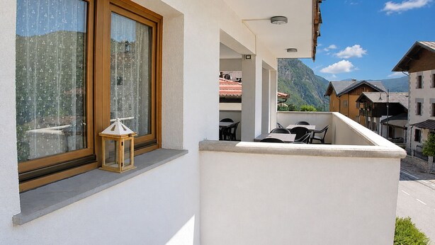 Un balcon avec une table et des chaises, une fenêtre avec des rideaux et une vue sur la montagne.