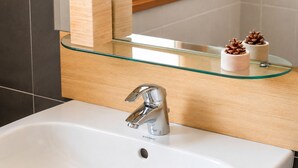 Une salle de bain avec un lavabo blanc, un robinet moderne, une étagère en verre avec des récipients en bois et des pommes de pin.
